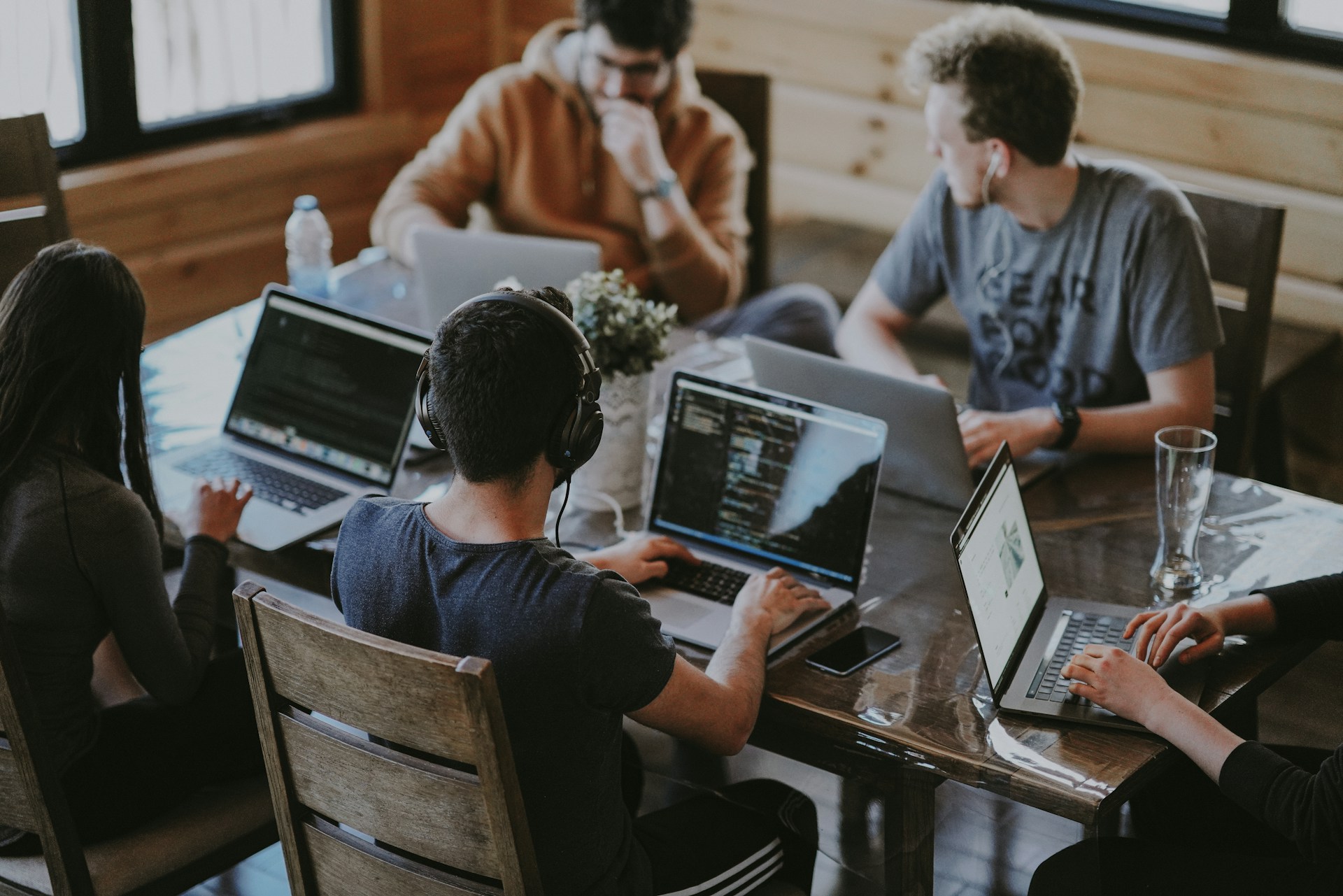 A group of people are sitting around a table with laptops, working on their computers.